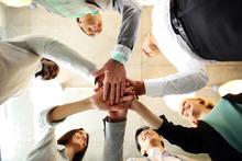 Team members smiling with hands together in a huddle, with the camera angled below their hands.