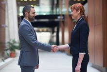 Two people dressed in business attire face each other and shake hands. 